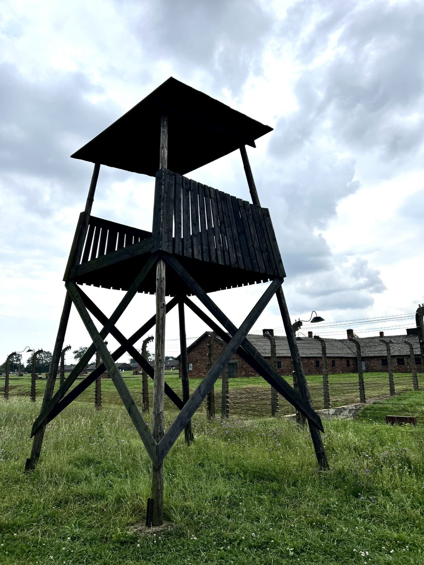 Wachturm und Stacheldraht in Auschwitz-Birkenau unter bewölktem Himmel
