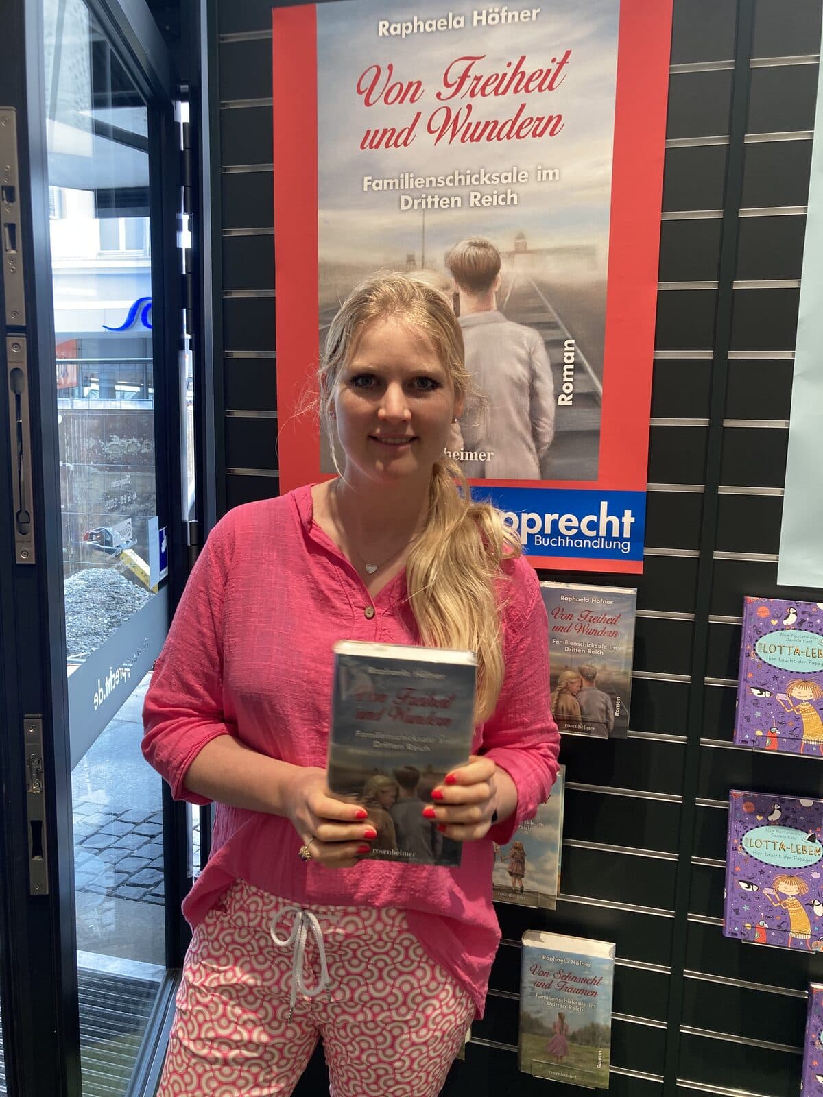 Raphaela Höfner mit „Von Freiheit und Wundern“ vor dem Plakat in der Buchhandlung